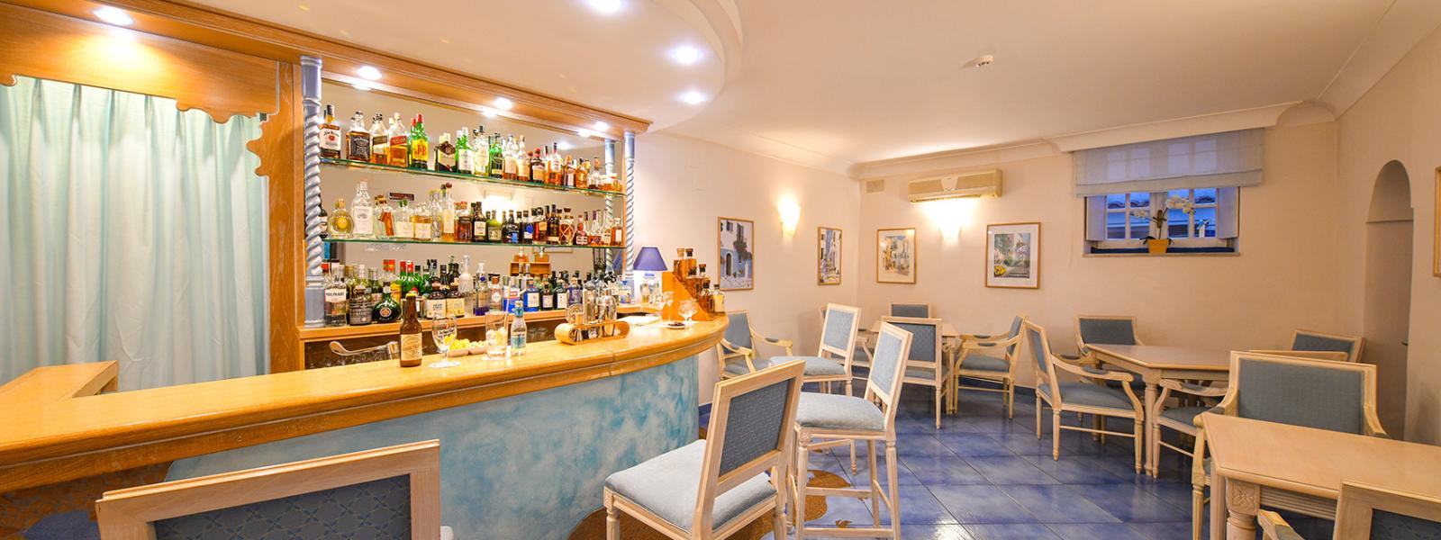 Elegante bar con sedie azzurre, illuminazione soffusa e vari liquori esposti.
