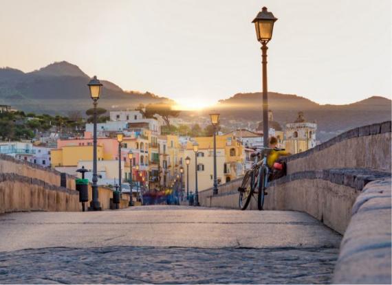 Tramonto su una strada con lampioni e case colorate, una bicicletta appoggiata al muro.
