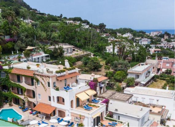 Vista panoramica di case su una collina con vegetazione e piscina, vicino al mare.