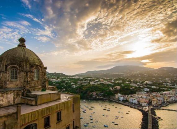 Vista panoramica su Ischia al tramonto, cupola e mare con barche.