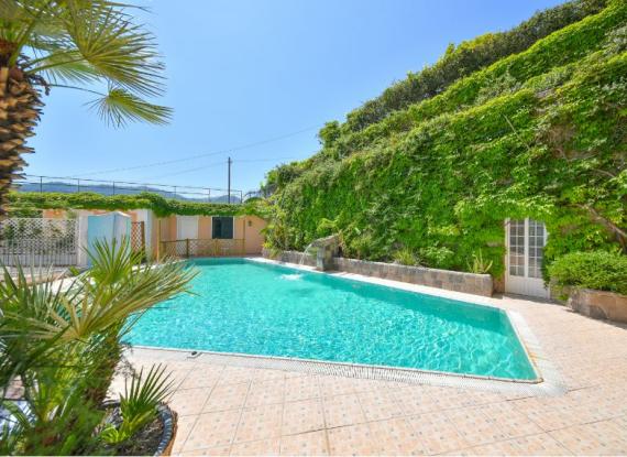 Piscina all'aperto circondata da verde, con cielo limpido e soleggiato.