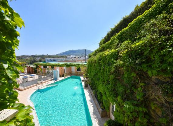 Piscina all'aperto con vista su colline, circondata da vegetazione lussureggiante.