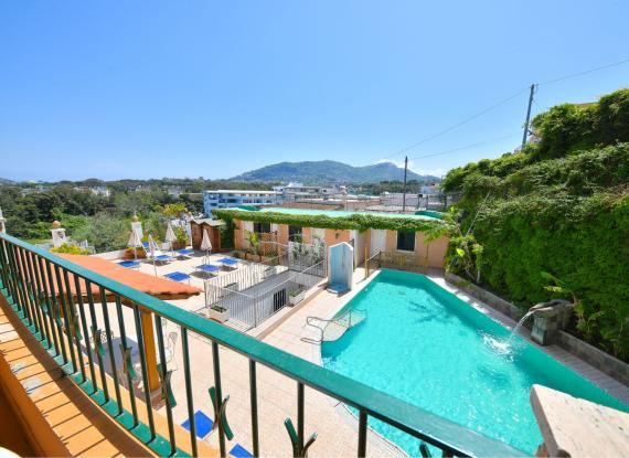 Piscina all'aperto con vista montagna, lettini e ombrelloni su terrazza soleggiata.