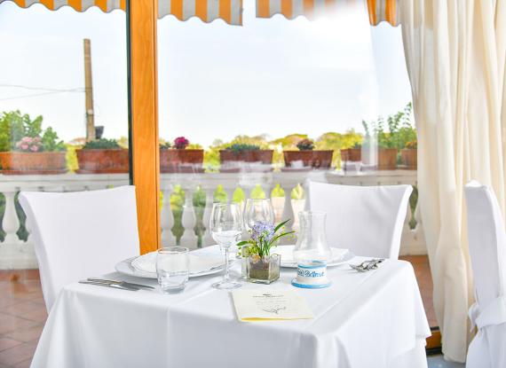 Tavolo apparecchiato in un ristorante elegante con vista su piante e balcone.