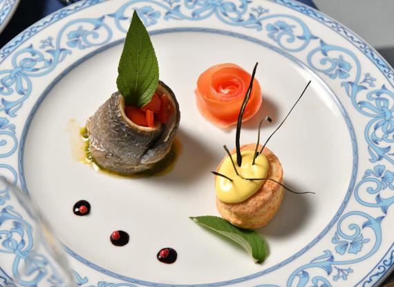 Piatto elegante con pesce, rosa di salmone e crema gialla su sfondo bianco e blu.