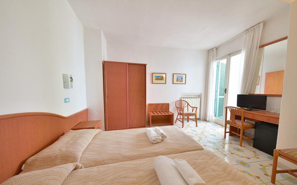 Camera accogliente con due letti, TV, balcone e arredamento semplice.