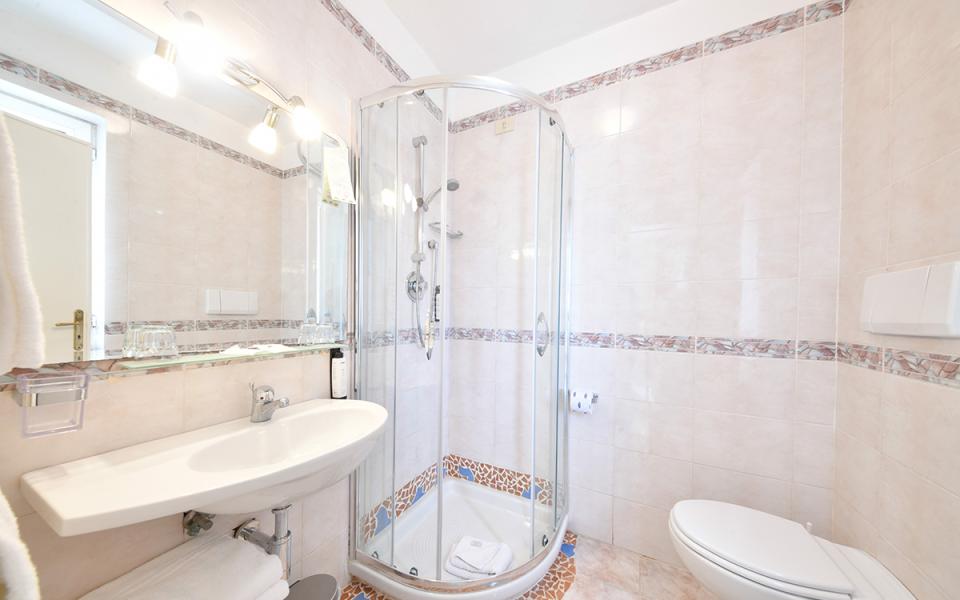 Bagno moderno con doccia angolare, lavandino sospeso e decorazioni in piastrelle colorate.