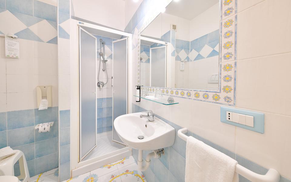 Bagno luminoso con doccia, piastrelle blu e bianche, e dettagli floreali.