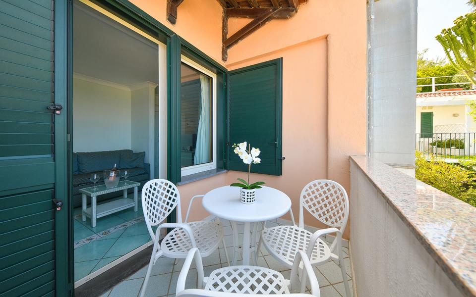Terrazza con tavolo bianco, sedie e pianta, vista su soggiorno con divano.