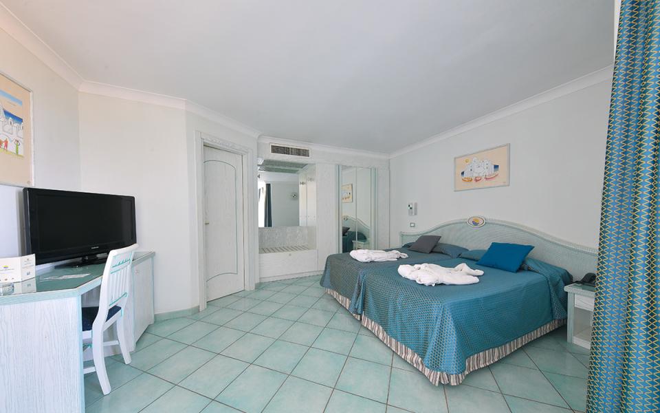 Camera d'albergo luminosa con letto matrimoniale, TV e arredi in tonalità blu.