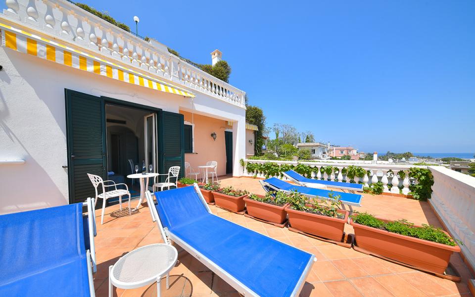 Terrazza soleggiata con lettini blu, tavolino e vista mare.