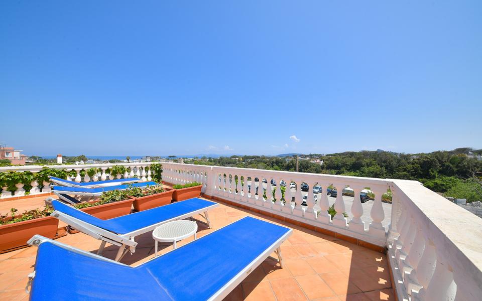 Terrazza con lettini blu, vista mare e cielo limpido.