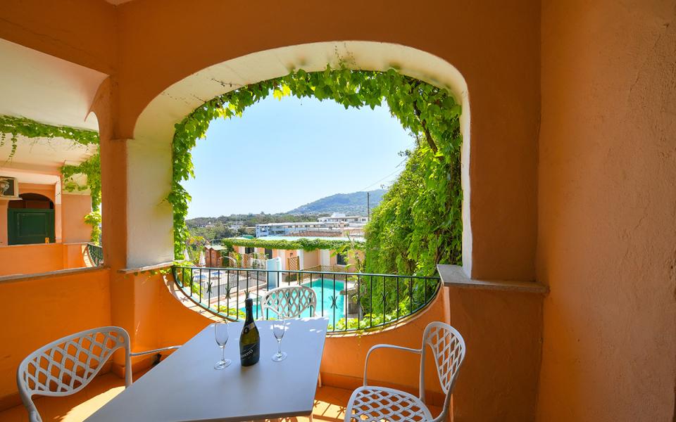 Terrazza con vista su piscina e colline, tavolo con bicchieri e bottiglia.